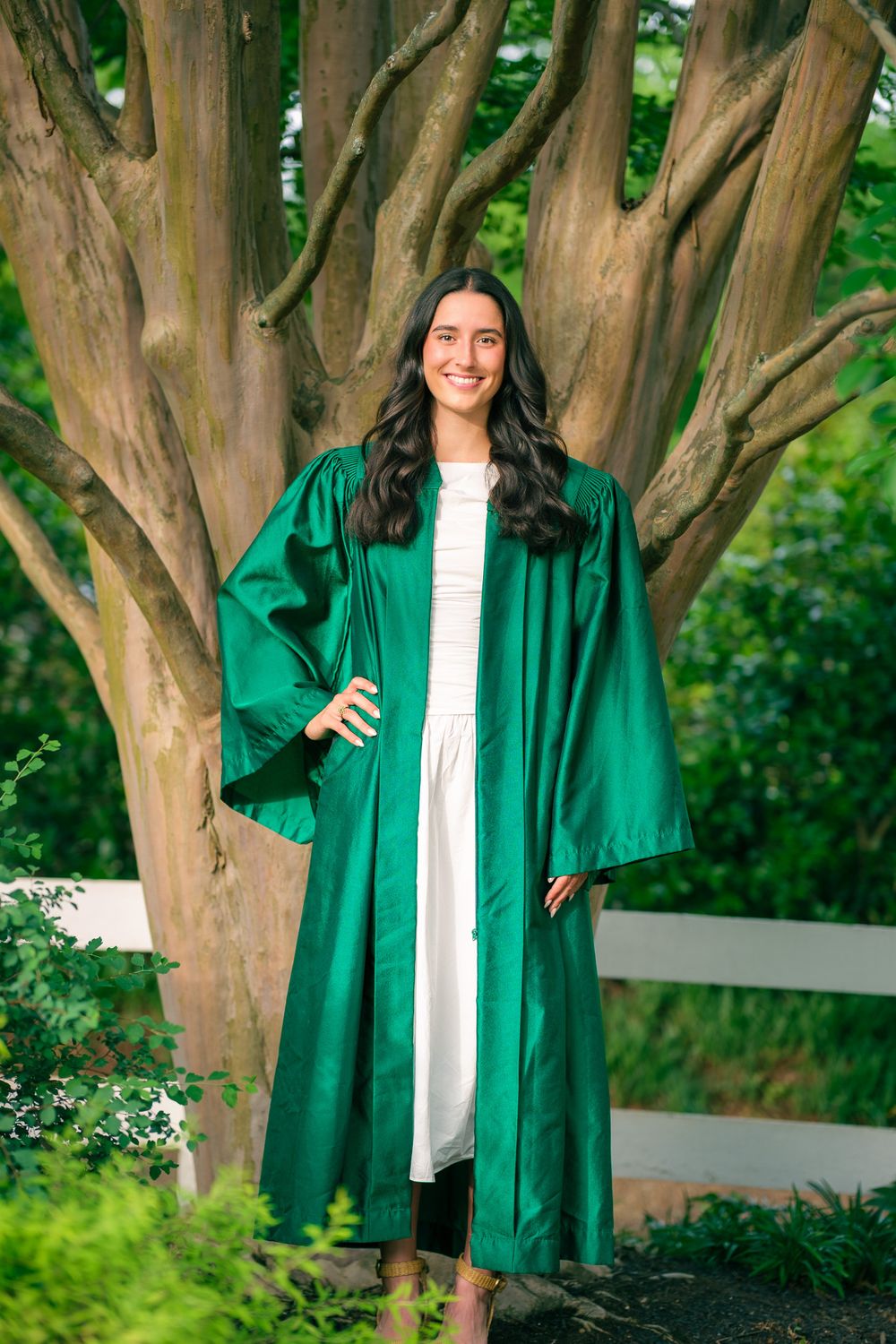 Senior cap and gown session photo session with graduate wearing a green graduation gown standing in front of a tree.