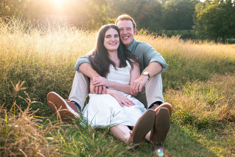 Couple sitting together in a sunny golden field, smiling warmly, perfect for engagement or love photography.