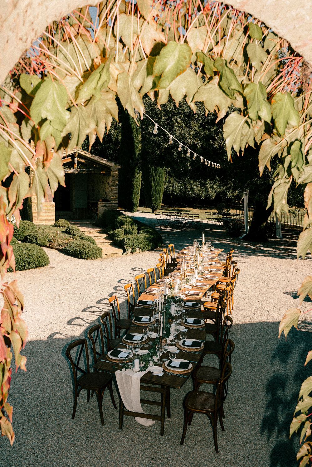 Elegant outdoor wedding reception table set under a stone arch with lush greenery at a rustic vineyard venue.