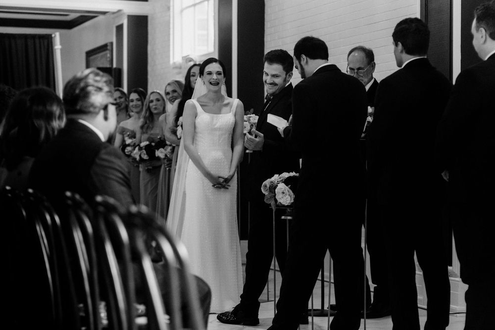 Filmic wedding ceremony photo of a laughing bride and groom at the altar surrounded by guests.
