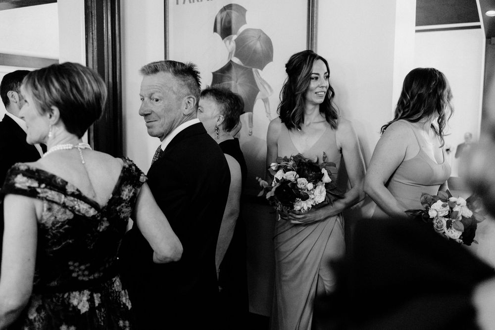 Artistic wedding photo of bridesmaids and wedding party gathered indoors, maid of honor holding bouquet smiling joyfully.