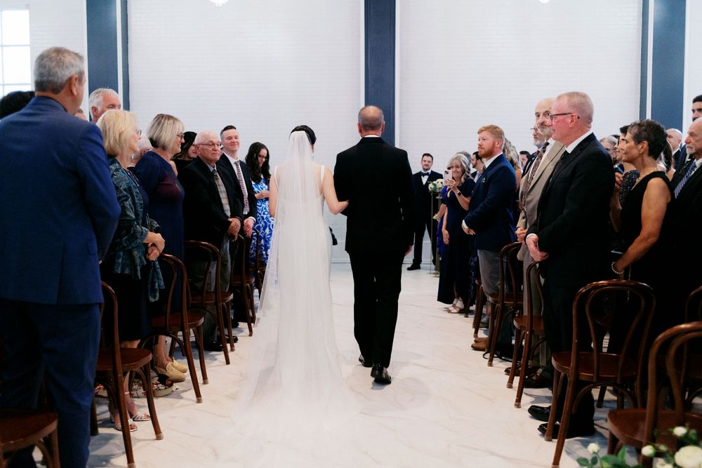 Milwaukee bride walking down the aisle with escort at refined wedding ceremony, guests seated in wooden chairs.