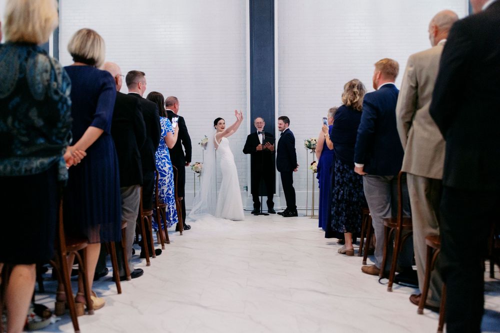 Bride celebrates at Wisconsin wedding ceremony altar as guests stand and applaud in elegant venue aisle.