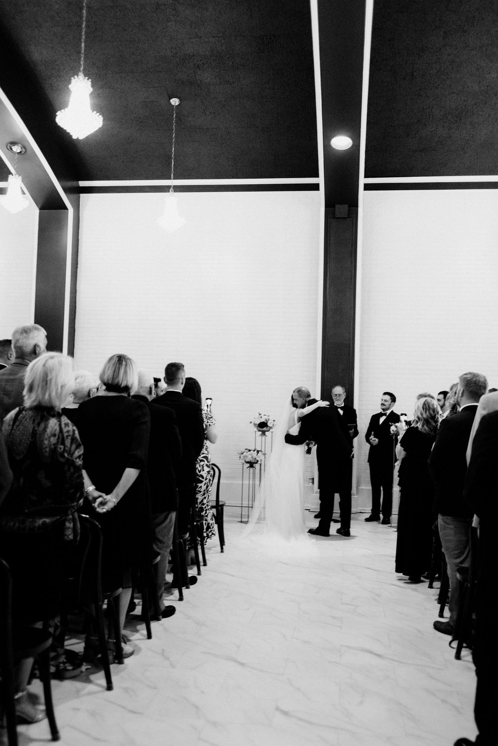 Emotional wedding ceremony photo showing bride hugging father at altar with seated guests in exquisite indoor venue.