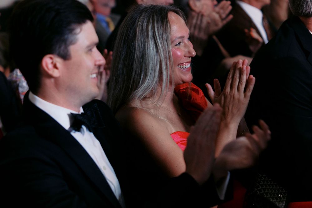 Elegant couple in formal attire clapping and smiling at a Victorian Milwaukee wedding, woman in red dress, man in tuxedo.