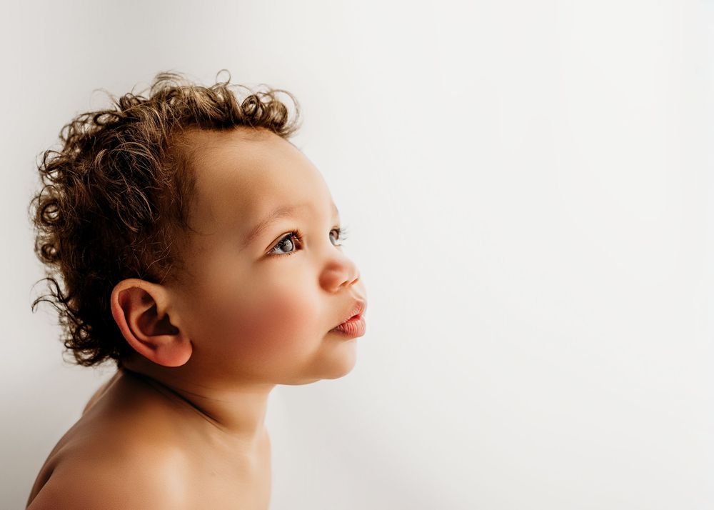 Curious mixed-race baby with curly hair looking up against a white background.