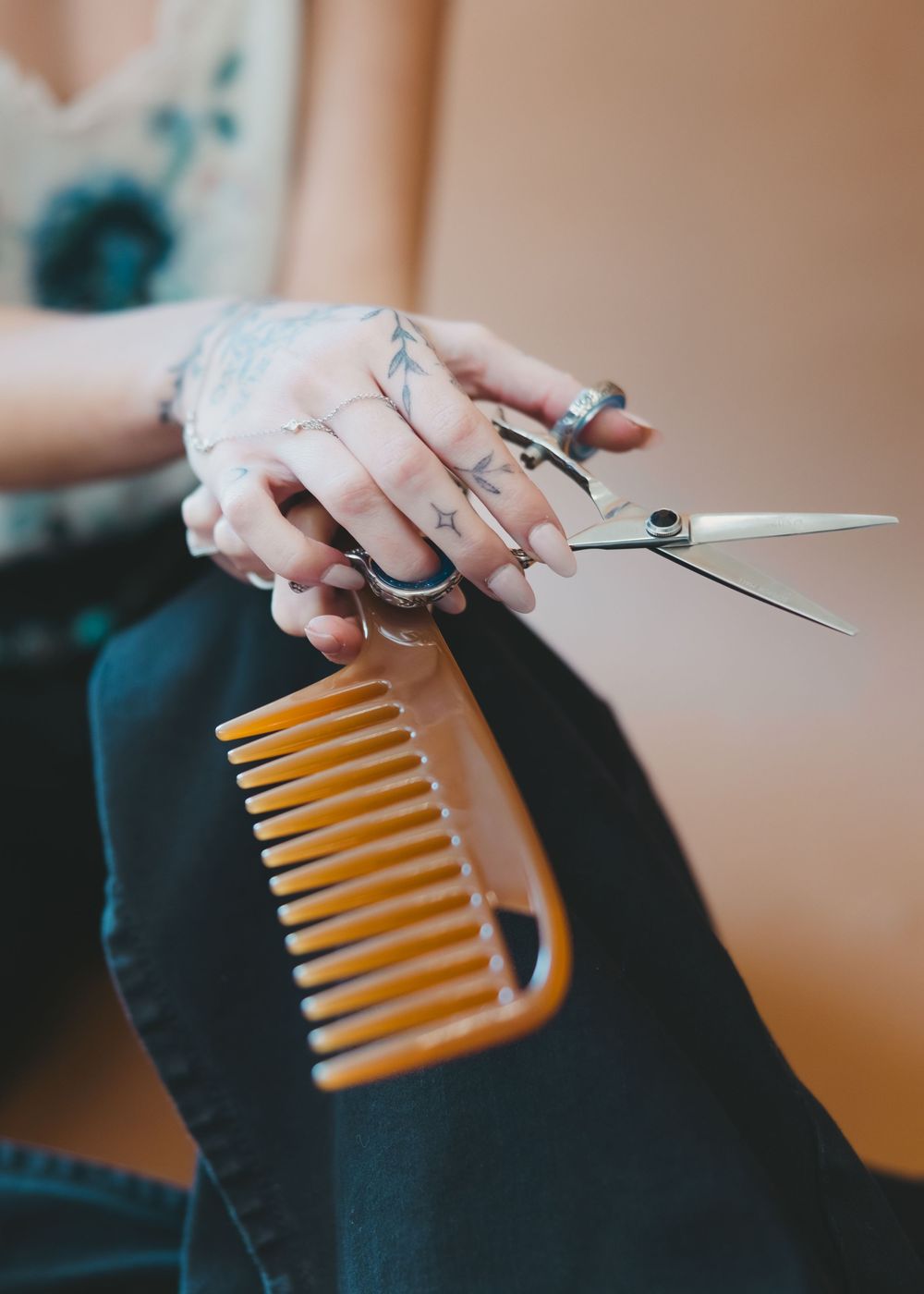 Tattooed hands holding professional hair scissors and wooden comb for hair styling.