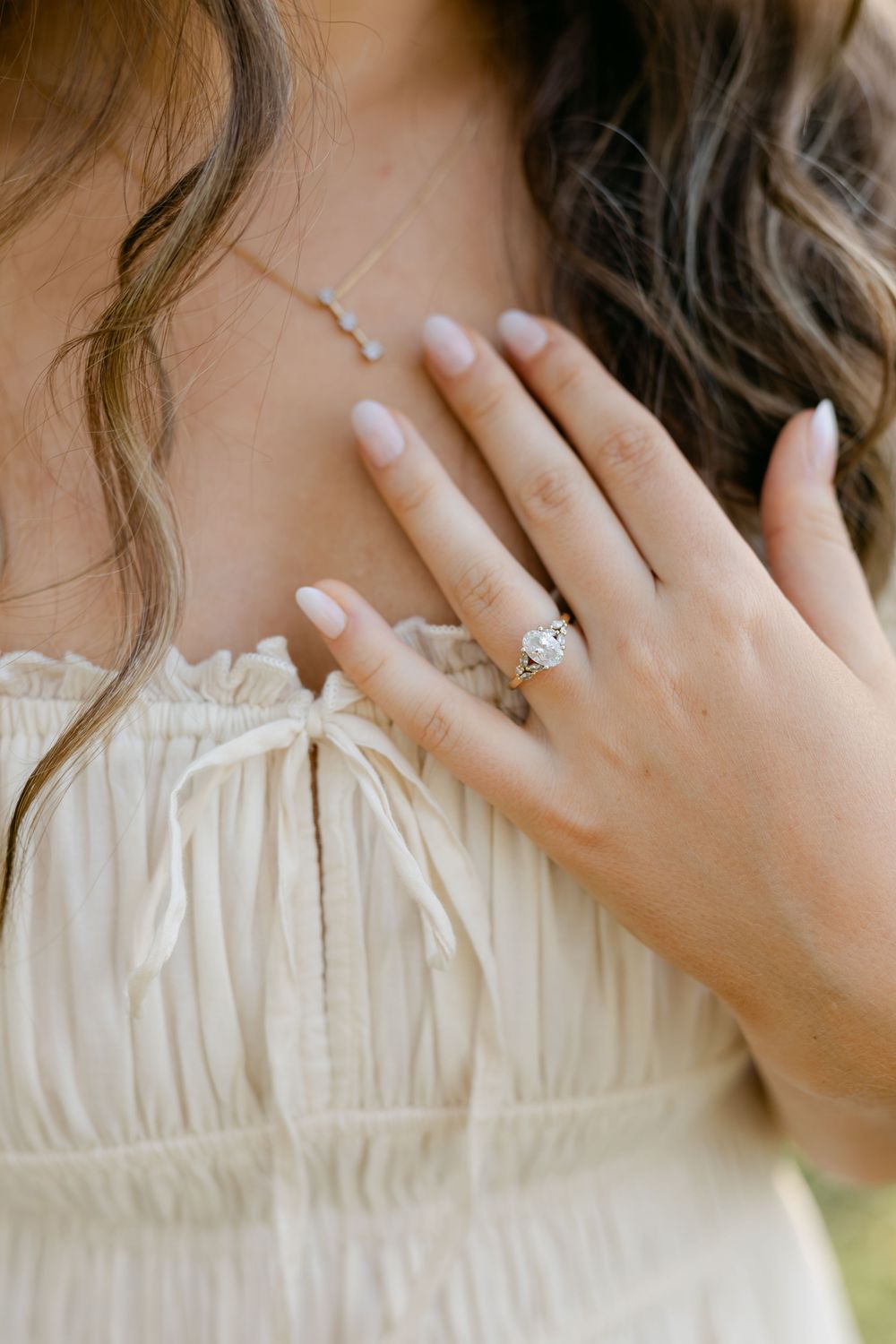 Close-up of a woman's hand showing a diamond engagement ring while wearing a cream dress.
