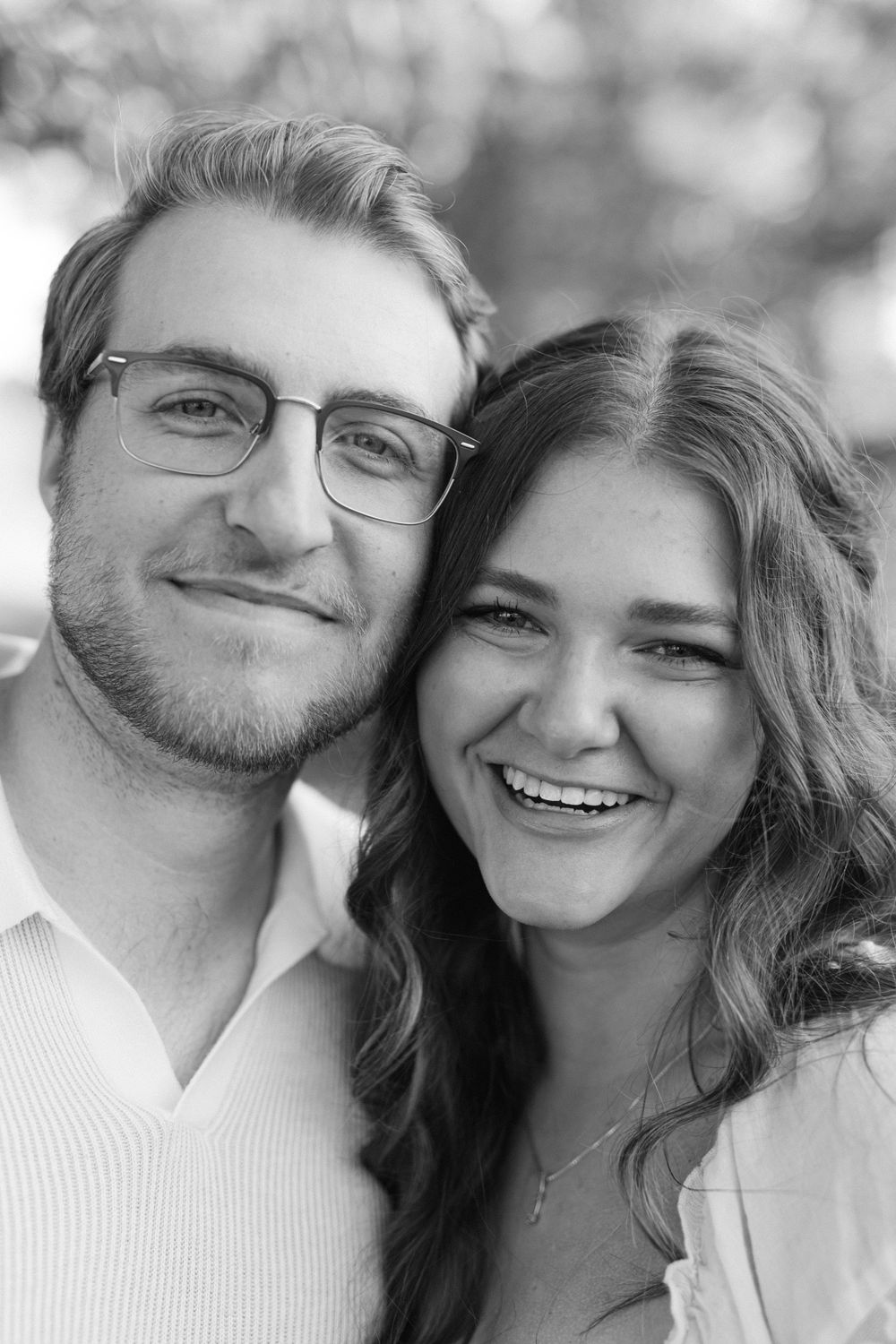 Black and white close-up portrait of a smiling couple cheek to cheek outdoors.