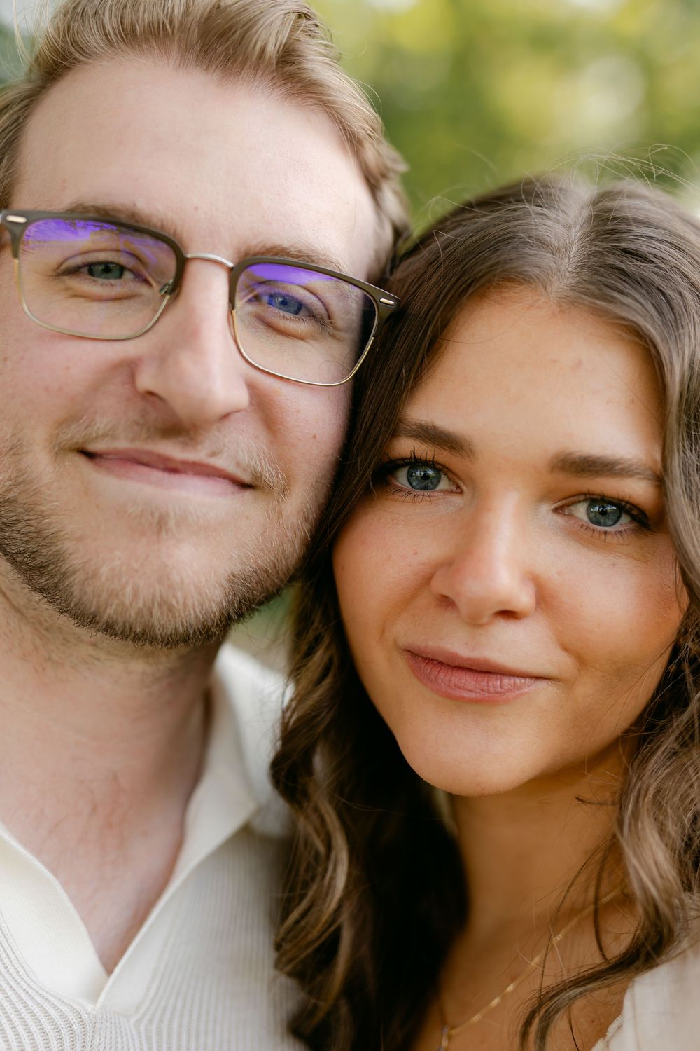 Close-up portrait of a young couple smiling softly with a blurred green background.