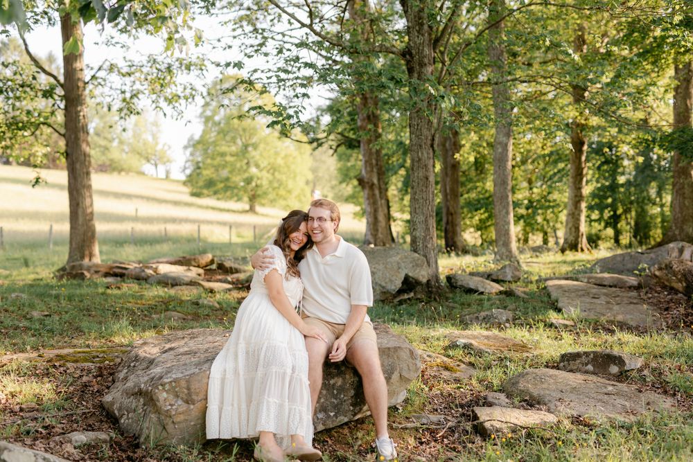 Happy couple sitting together on large rocks in a lush green wooded outdoor setting in natural light.