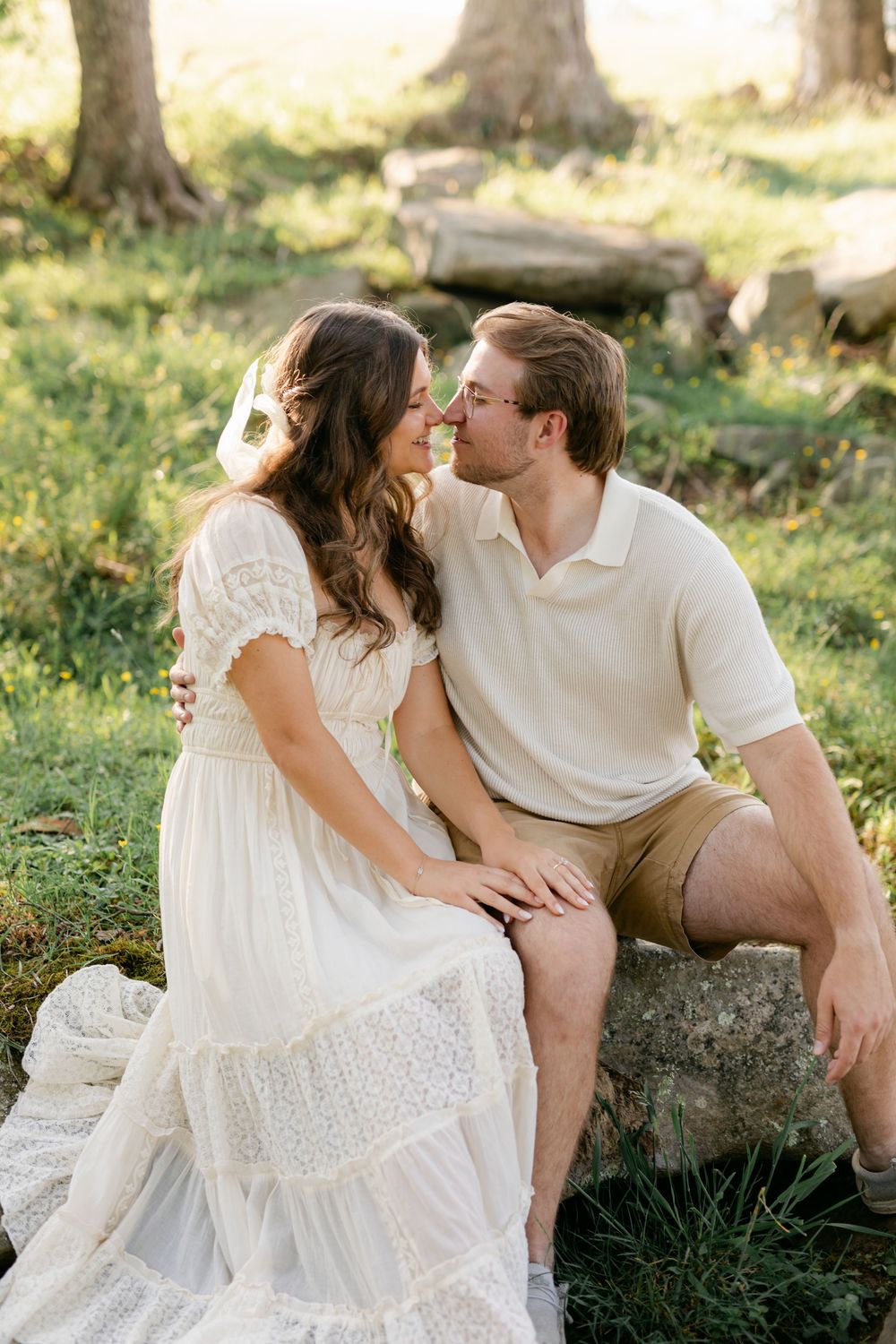 Couple leaning in for a kiss while seated on a rock in a bright green sunlit outdoor forest setting.