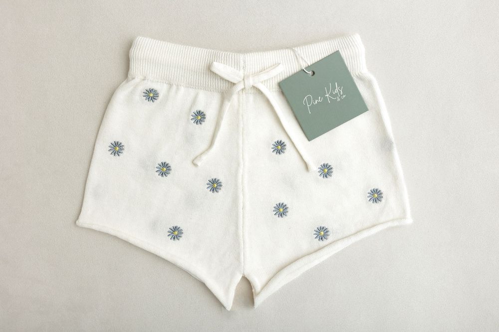 White kids shorts with blue floral embroidery and drawstring waist, displayed flat with a Fin Kids brand tag.