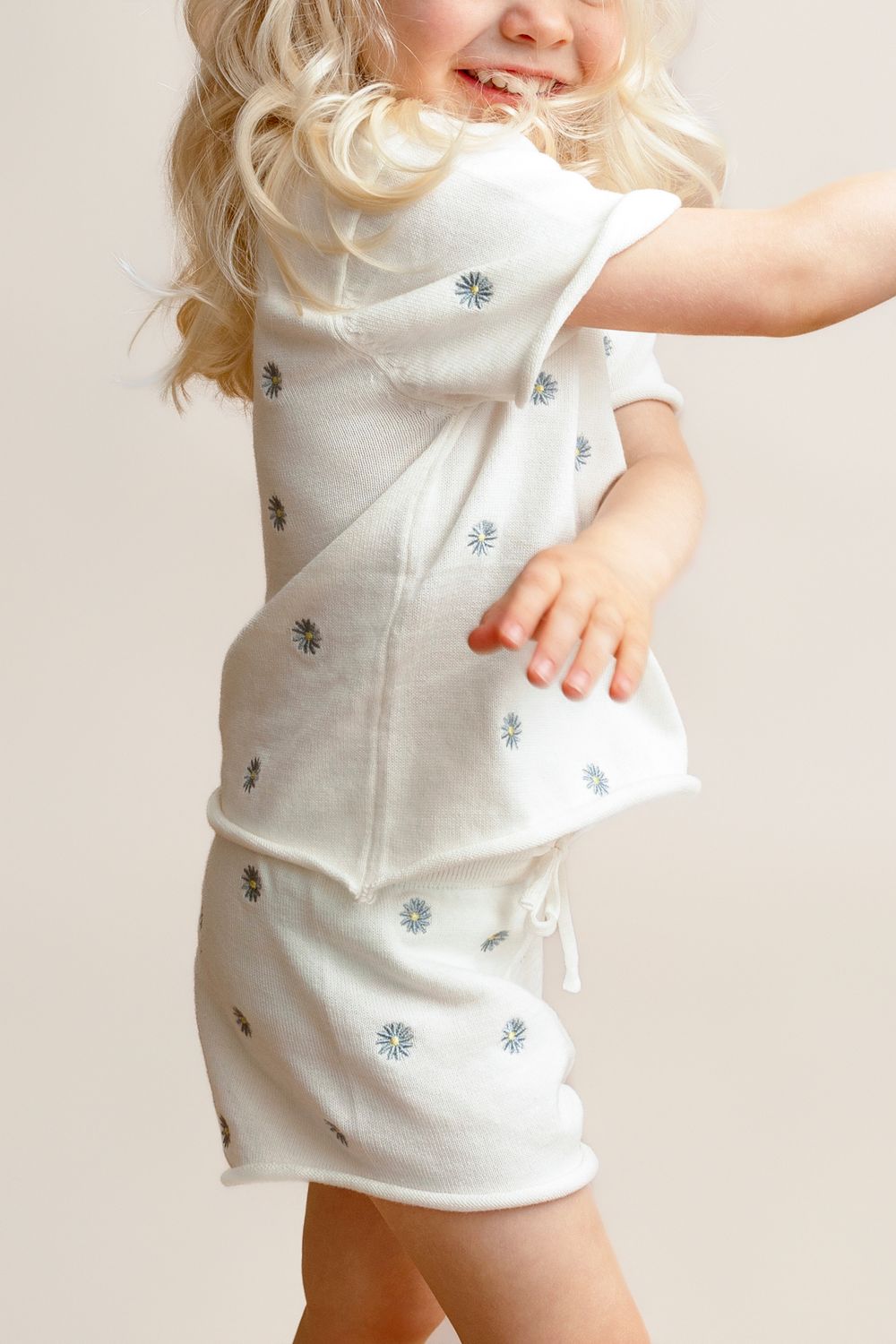 Toddler girl in white floral print short sleeve dress, smiling and spinning playfully.
