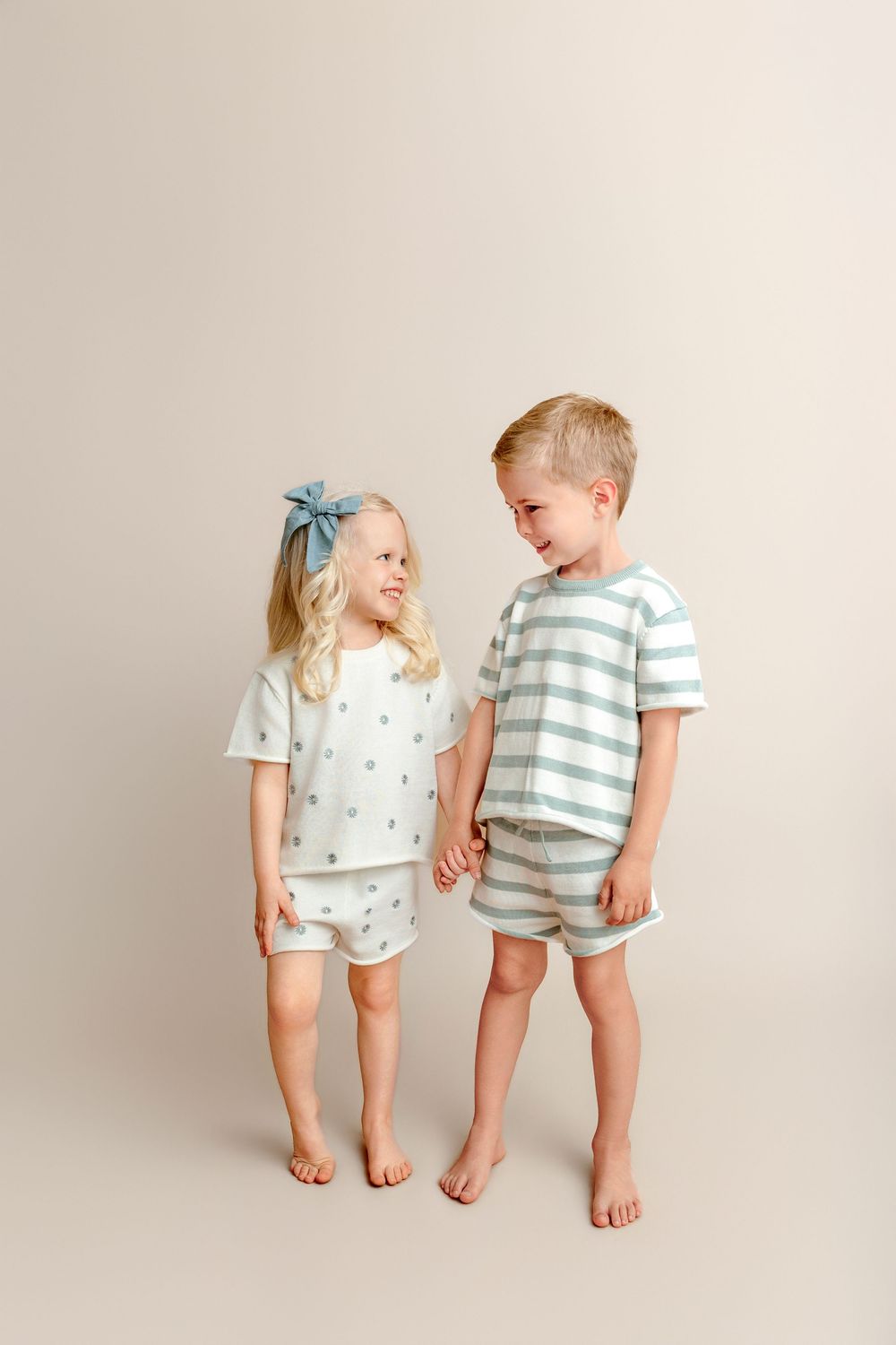 Two young children in matching pastel pajama sets smile at each other against a neutral background.
