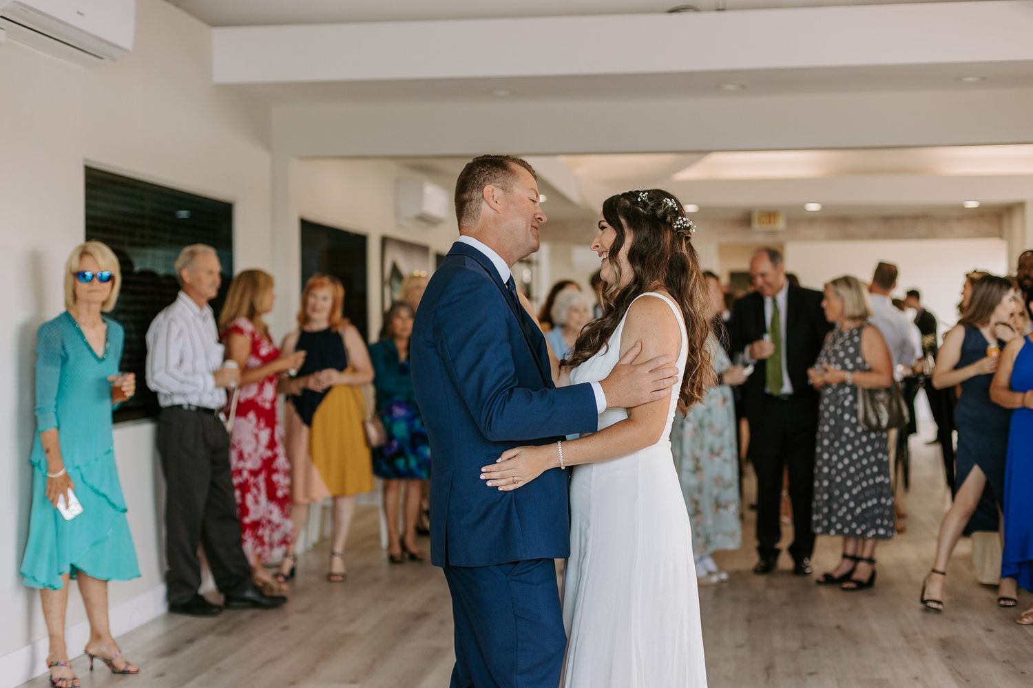 Bride and groom share their first dance surrounded by guests at a wedding reception.