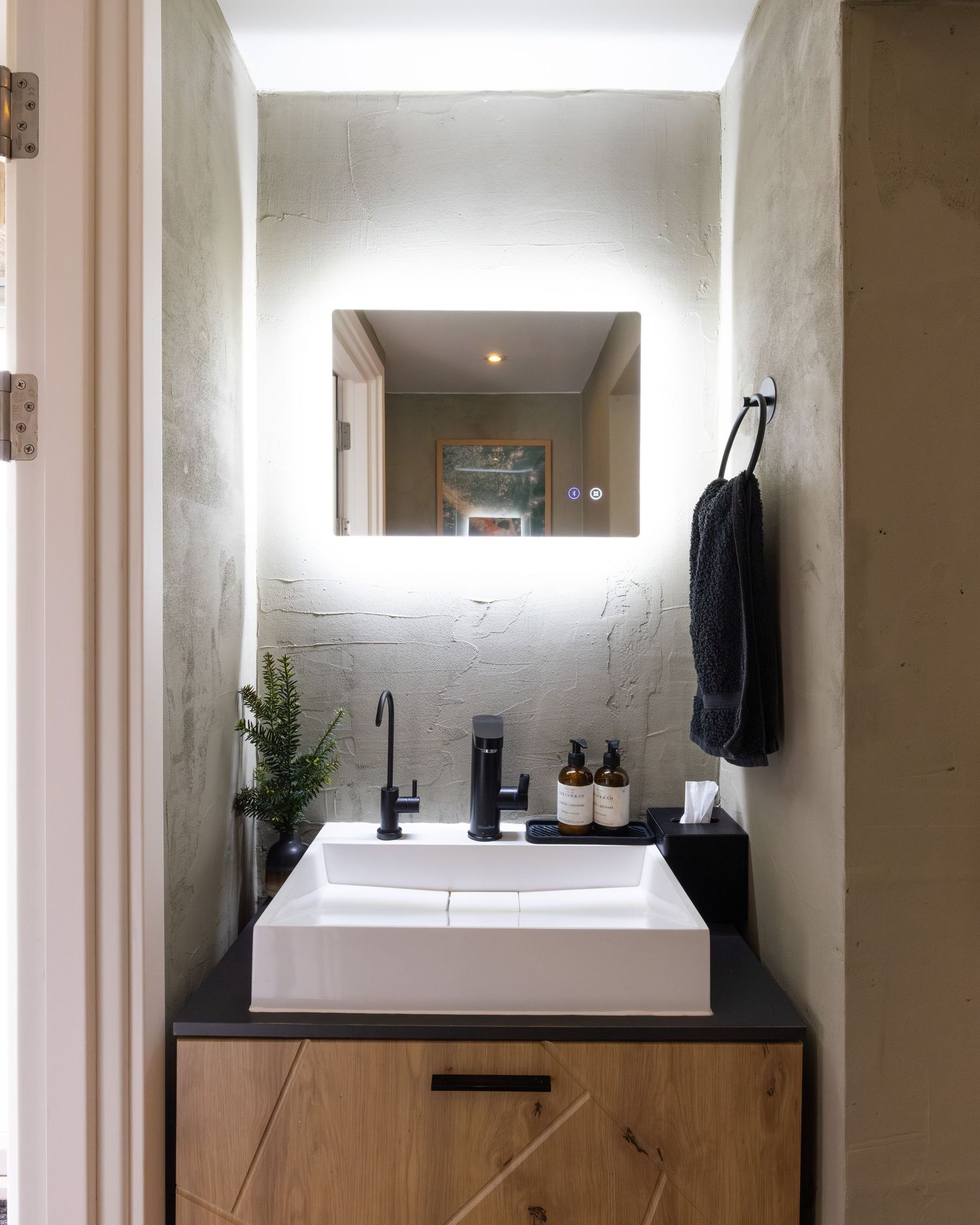 Modern spa bathroom in Bedfordshire with backlit mirror, vessel sink and black tap on wood vanity, interior shoot.