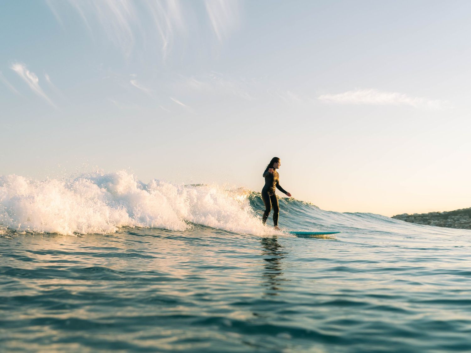 female surfer at Bar Beach Newcastle NSW with soft sunset light surfing into the sun with her reflection on the wave below