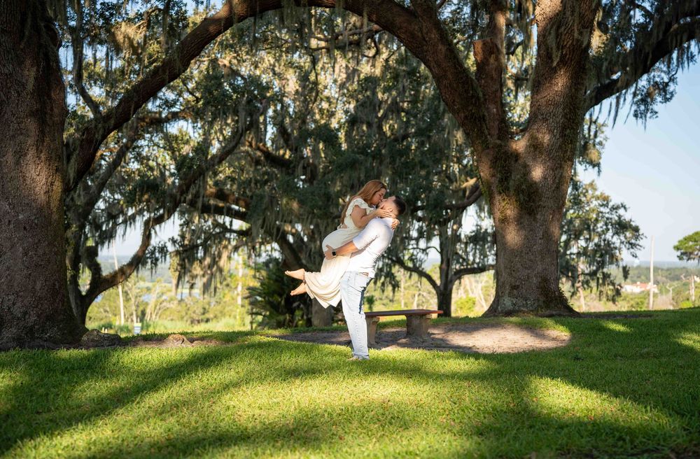 Couple embracing under sprawling oak trees draped with Spanish moss on a lush green lawn.