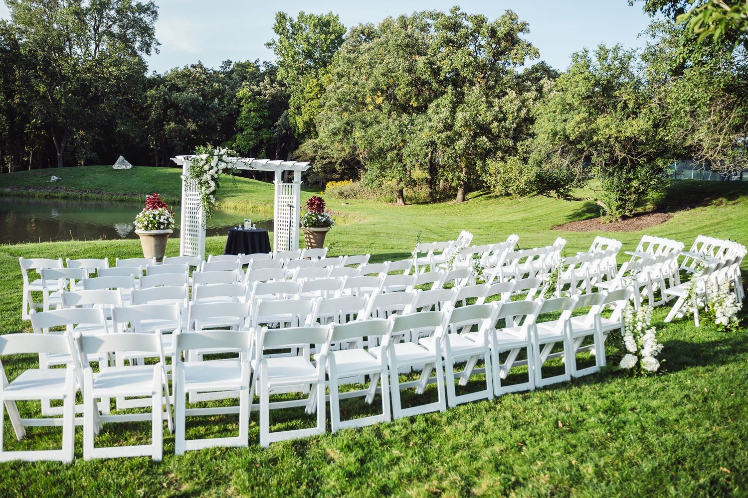 Bride and groom walk down outdoor aisle after wedding ceremony on lush green lawn with guests seated in white chairs.