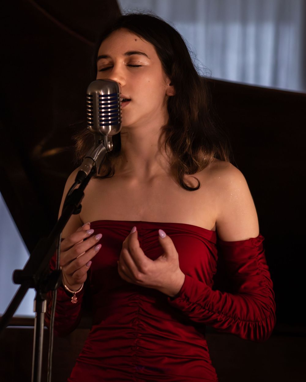 Woman in red off-shoulder dress singing passionately into a vintage microphone on stage.