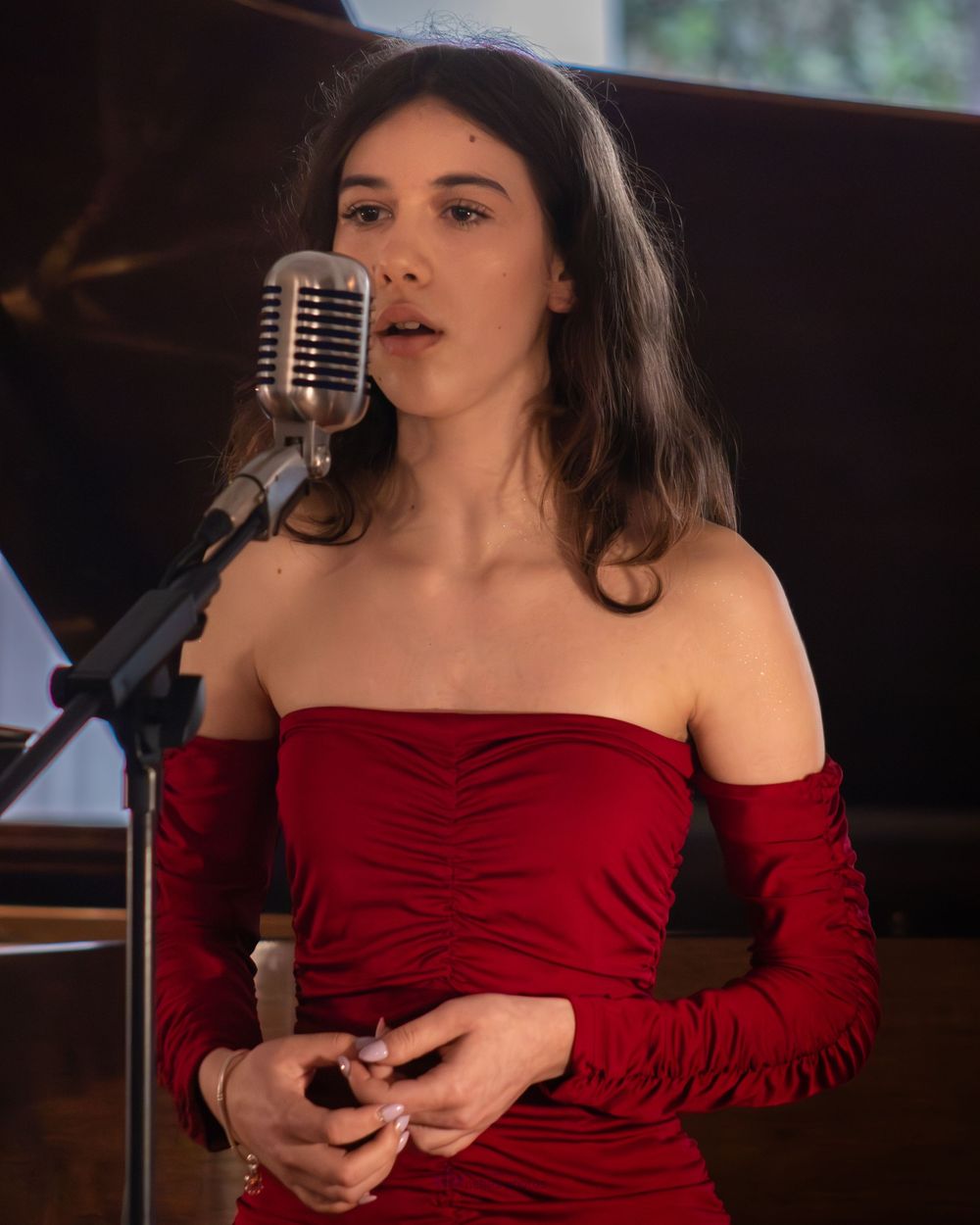 Woman in red off-shoulder dress singing into a vintage microphone at a live music performance.