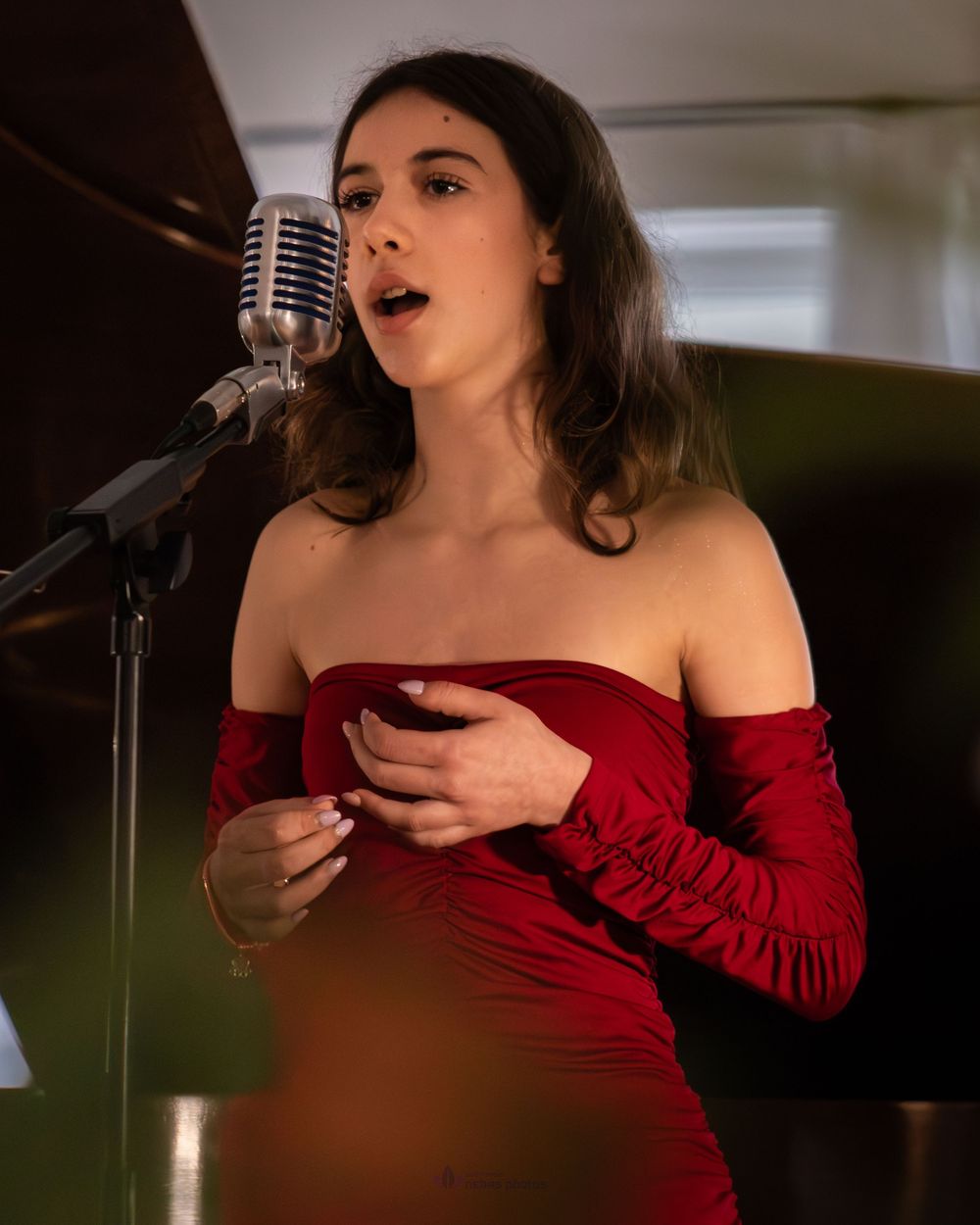 Woman in red off-shoulder dress singing into vintage microphone at live performance.