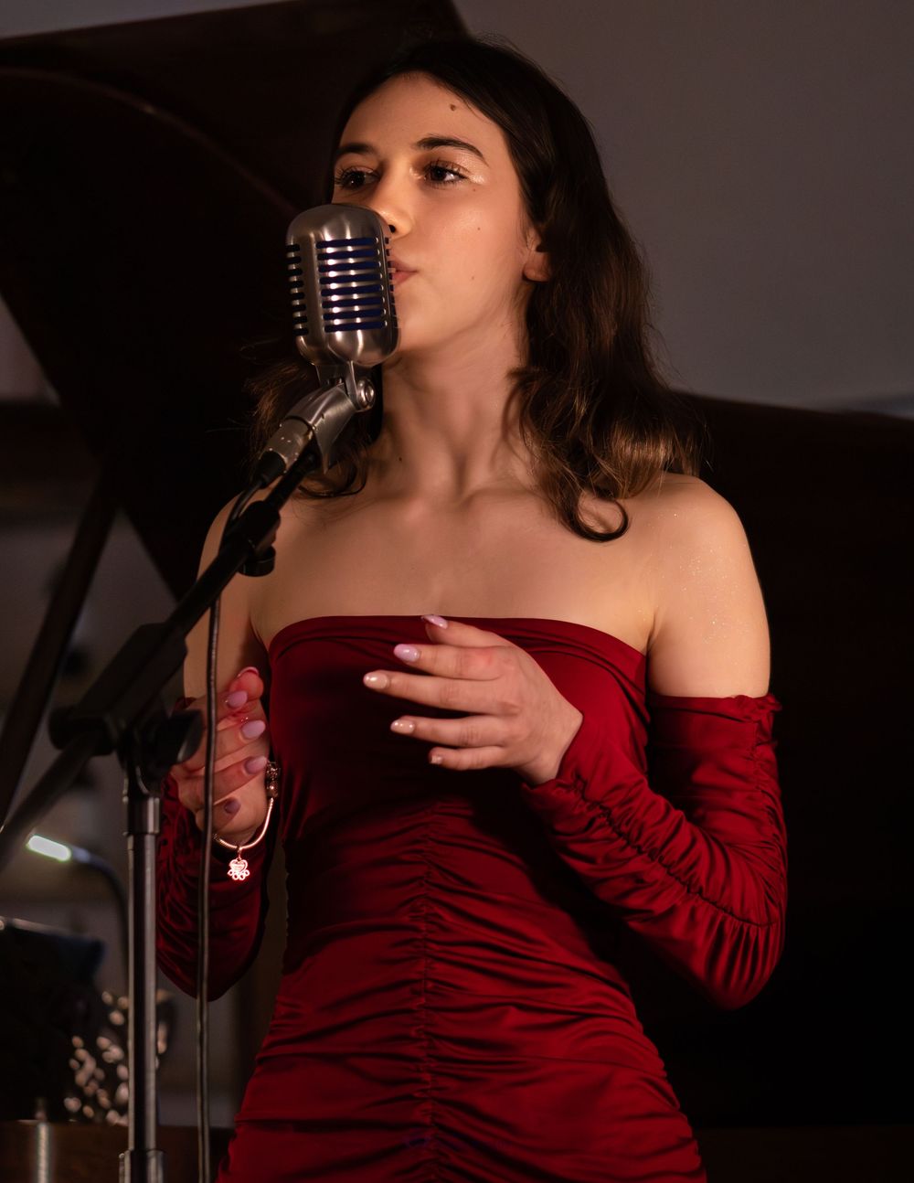 Woman in red off-shoulder dress singing into vintage microphone on stage.