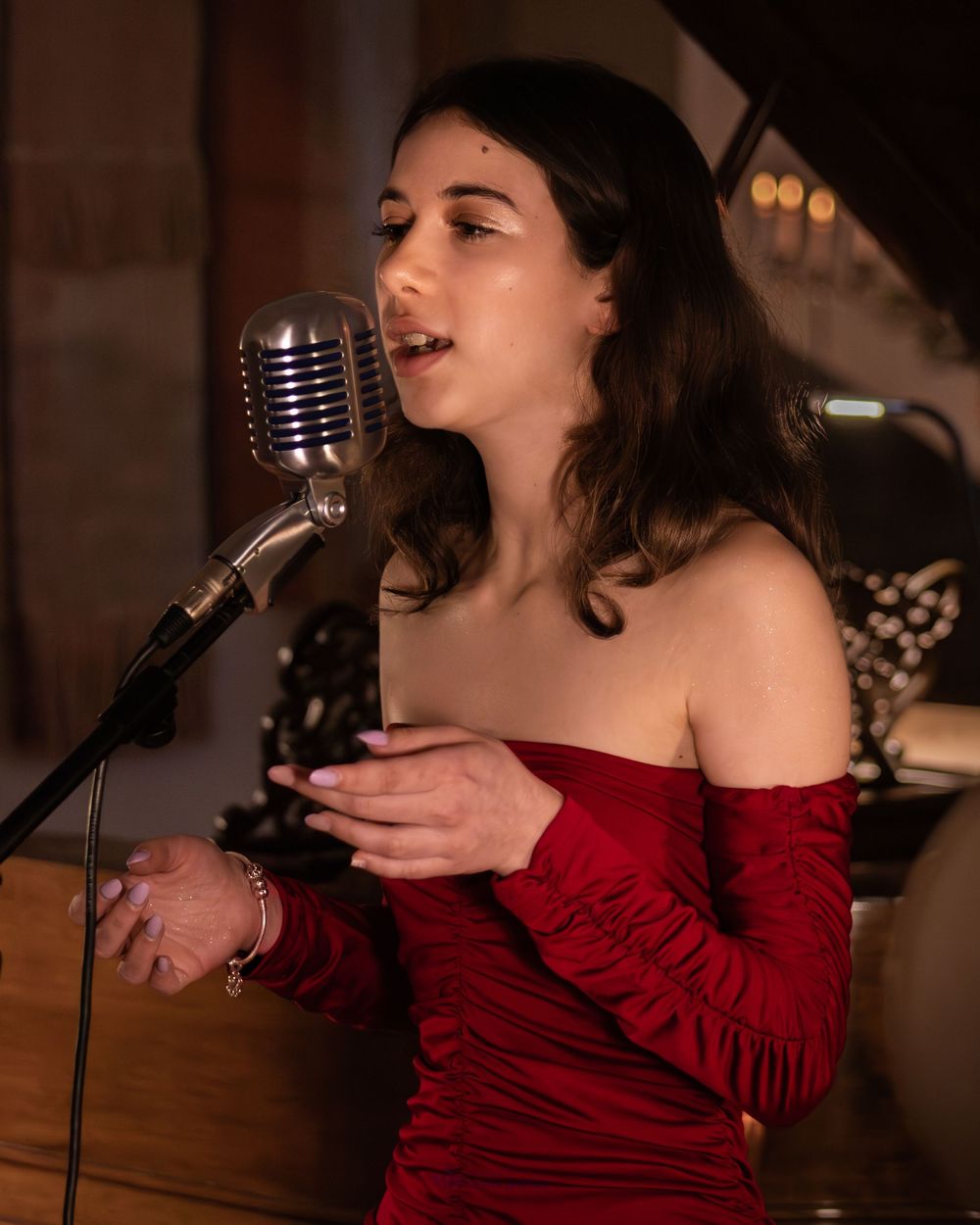 Young woman in red off-shoulder dress singing into vintage microphone at live performance event.