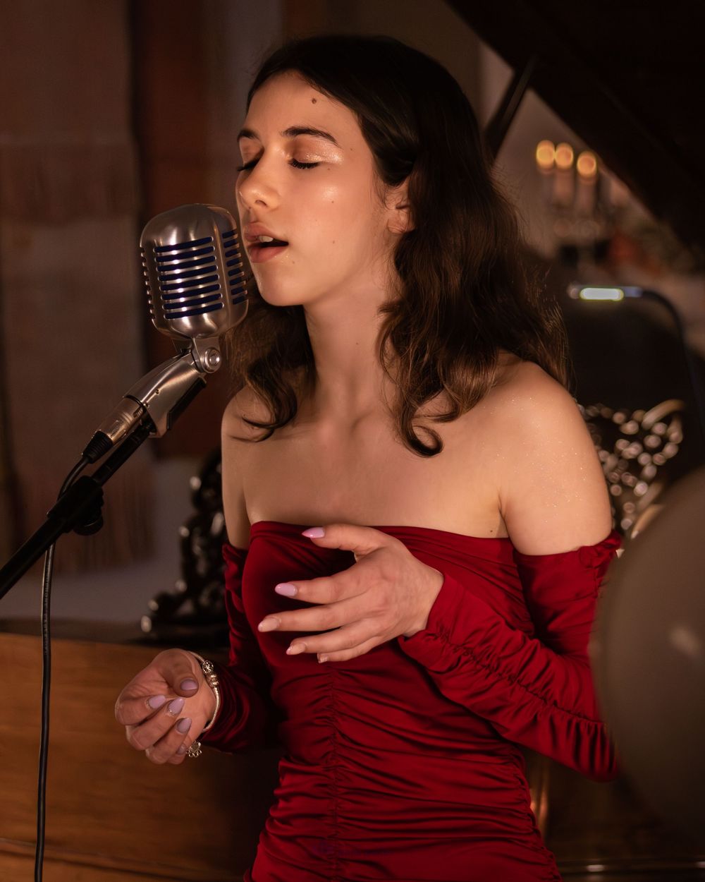 Female vocalist in red dress performing with eyes closed at retro microphone.