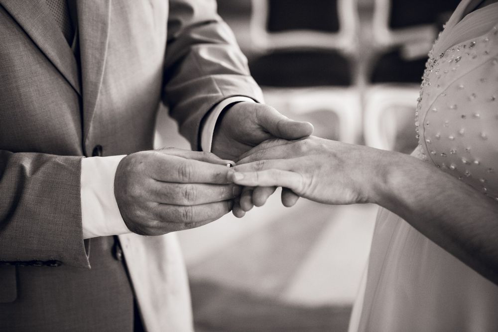 Groom placing a wedding ring on brides finger during an elegant ceremony, captured in black and white.