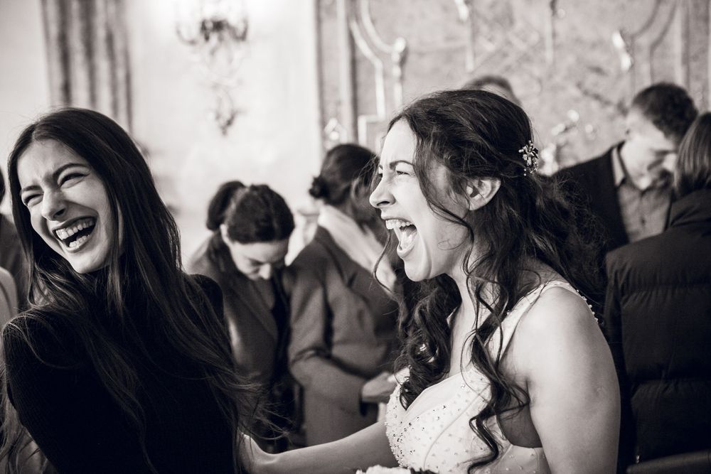 Black and white photo of bride and female guest laughing joyfully together during wedding ceremony reception.