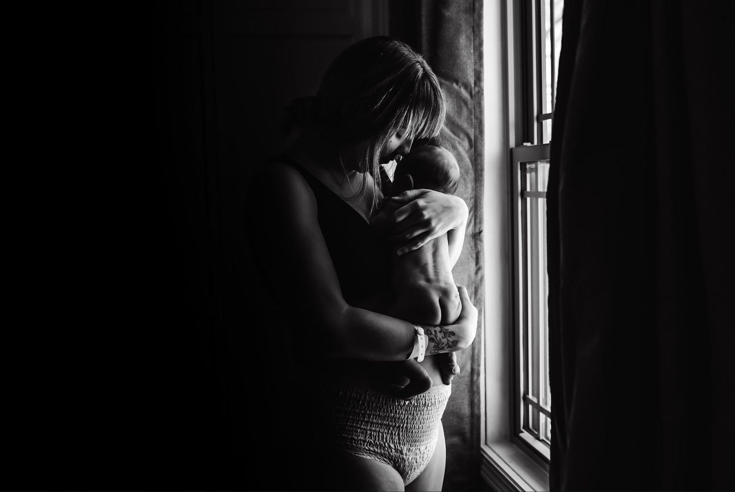 Silhouette by window shows quiet moment with newborn being held.