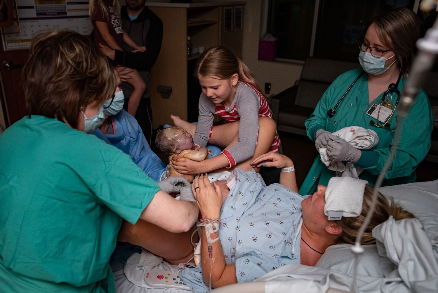 Medical staff assist with delivery while surrounding a hospital bed.