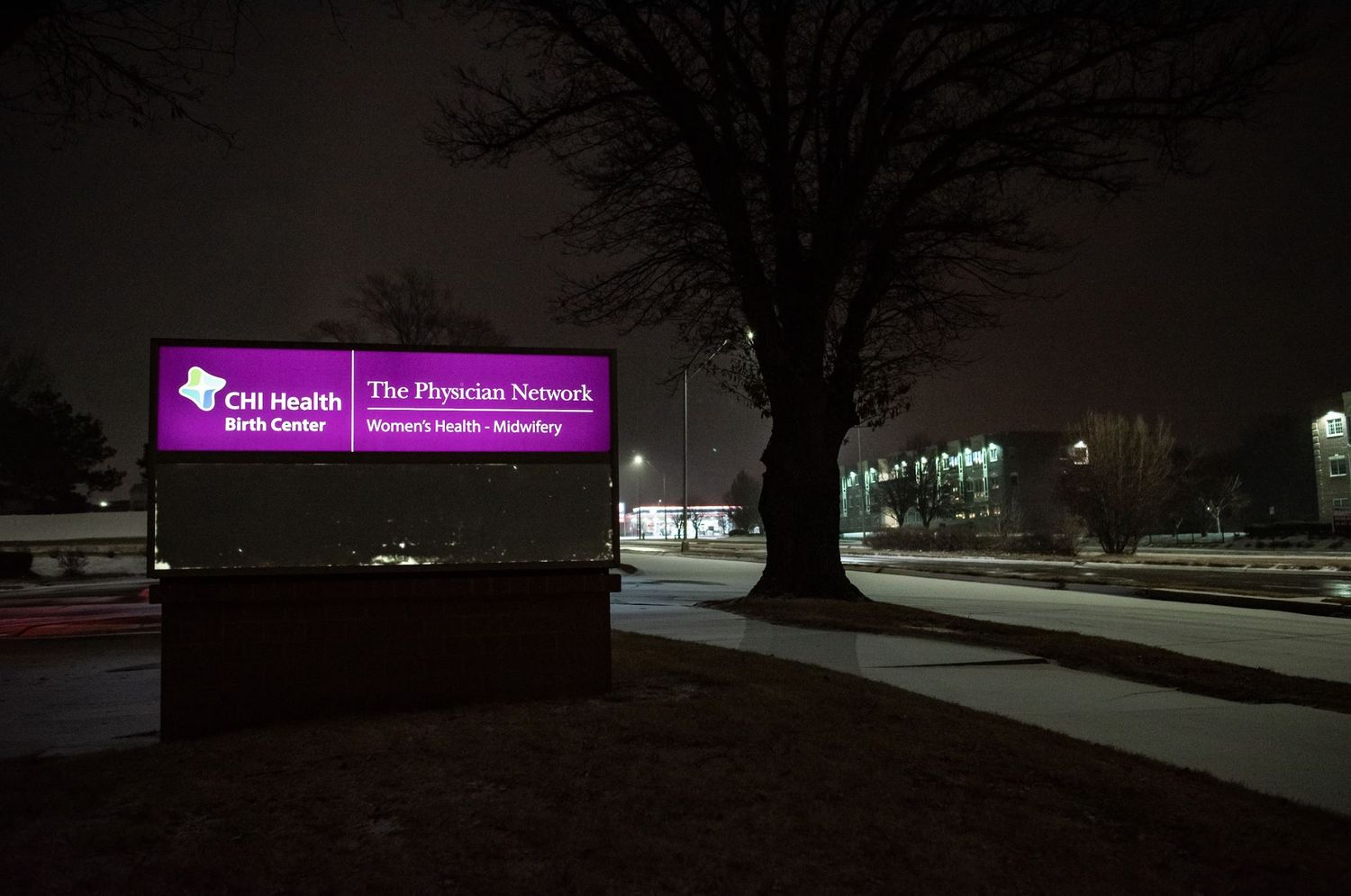 Illuminated hospital sign for The Physician Network glowing purple at night.