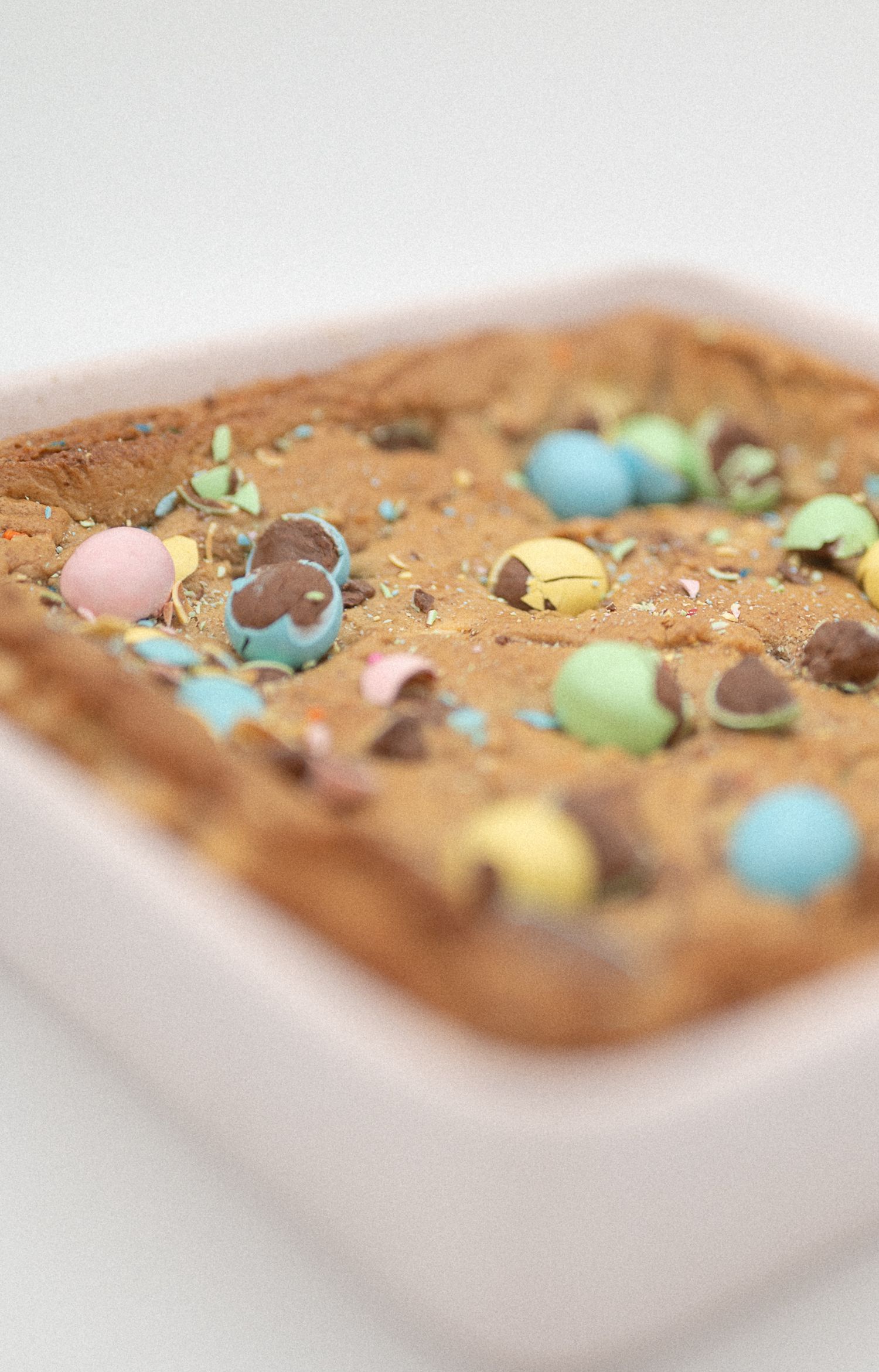 Easter cookie bars with colorful candy-coated chocolate eggs baked into golden brown blondie bars in a pink baking dish.