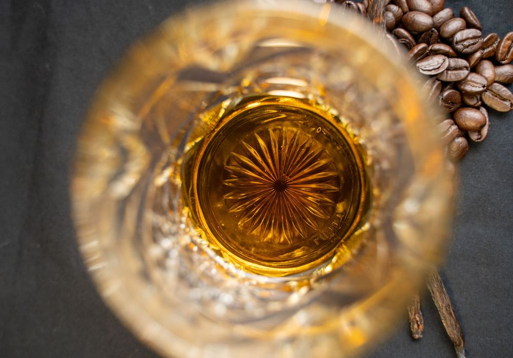 Coffee beans fall into a crystal glass creating a dynamic splash and reflection pattern in golden lighting.