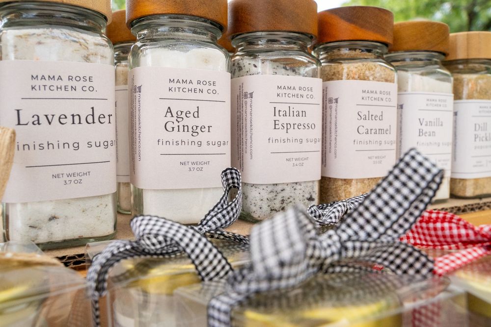 Glass jars with gingham ribbon decorations containing various spices and ingredients on wooden shelving.