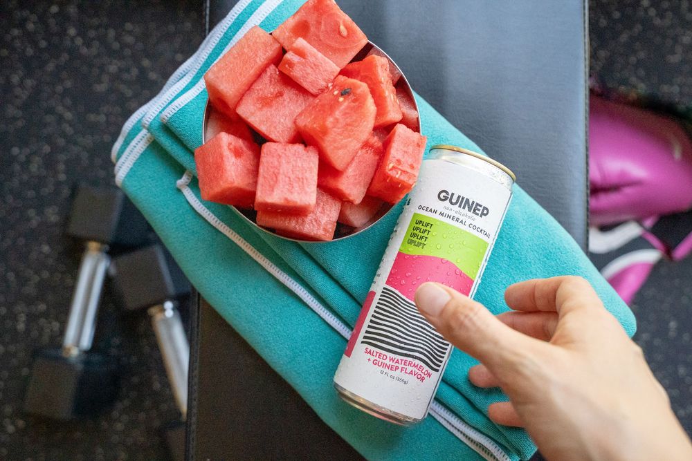 Fresh watermelon cubes on turquoise cutting board with product bottles.