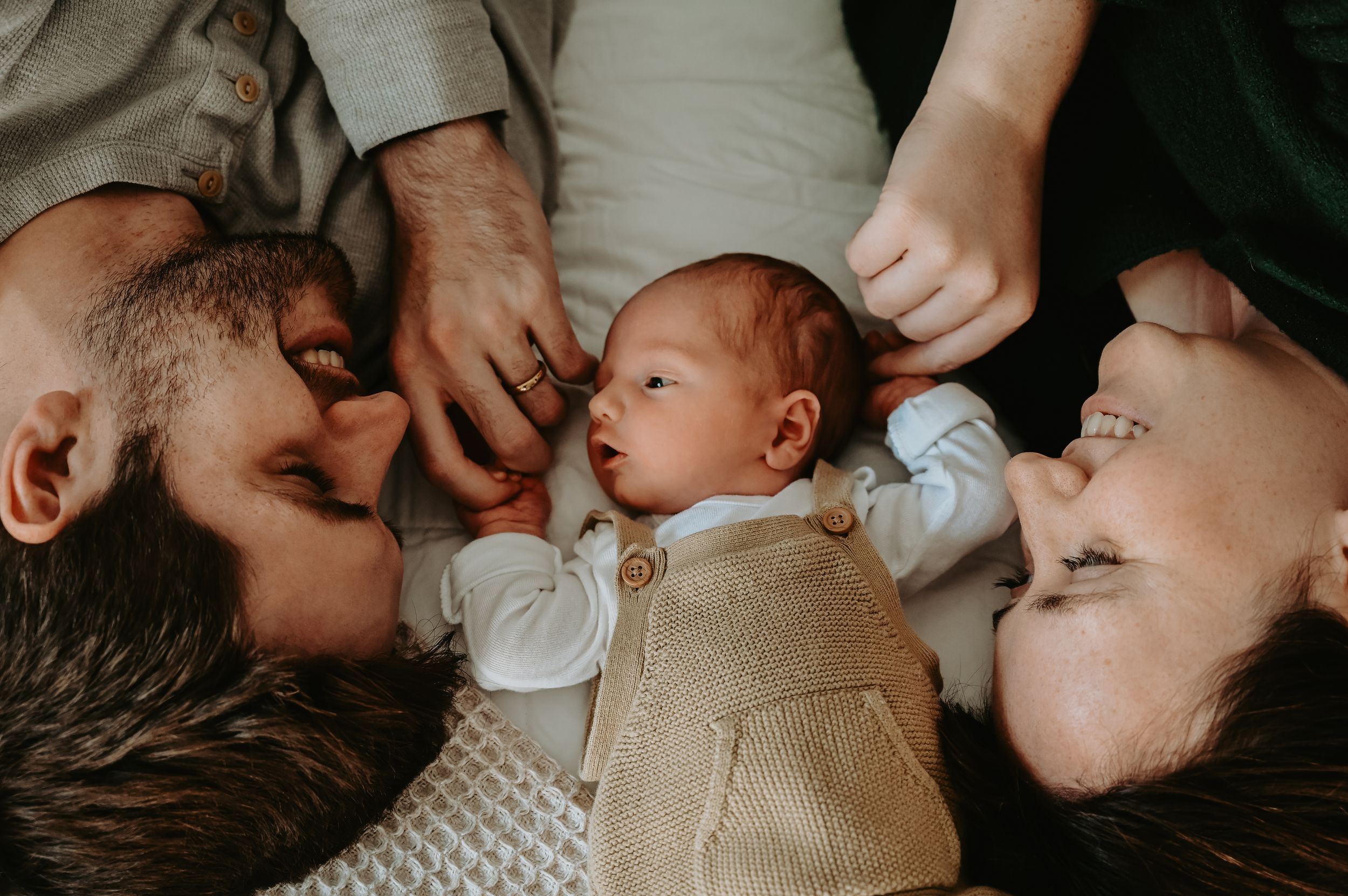 Two parents lying down with their newborn baby between them, sharing a tender family moment.