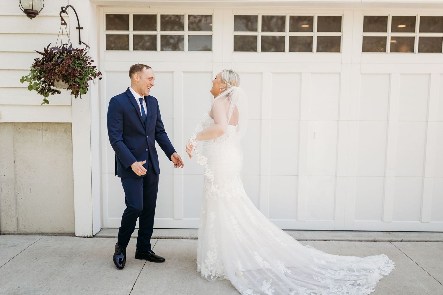 Bride and groom share a romantic first look moment outside a white building, bride in lace gown, groom in navy suit.