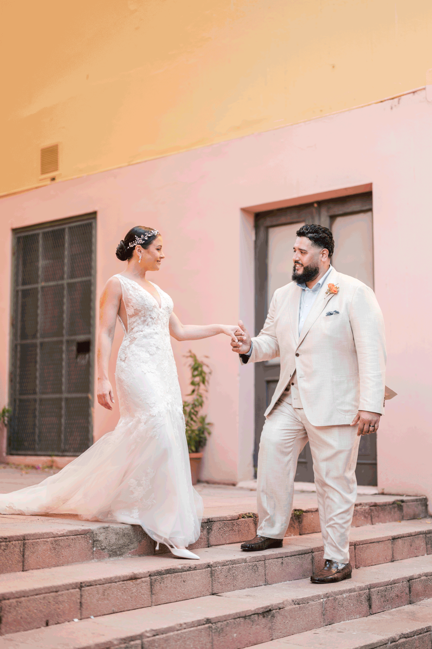 Bride and groom walking down elegant steps in pastel architecture setting