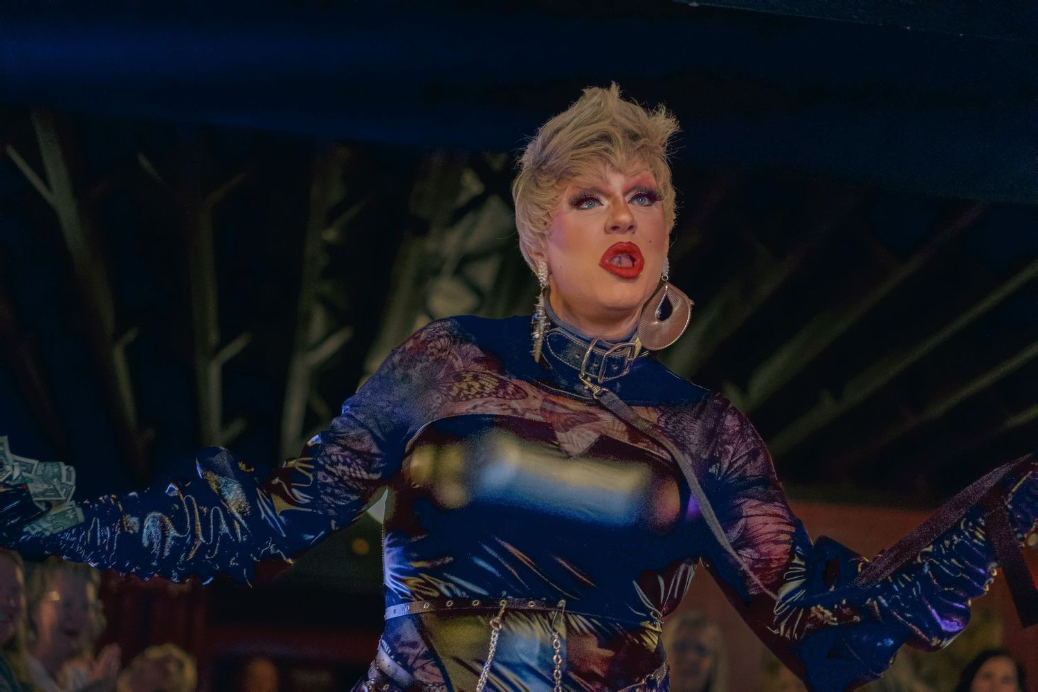 Drag performer in blue sequined outfit dancing on stage under dramatic lighting.