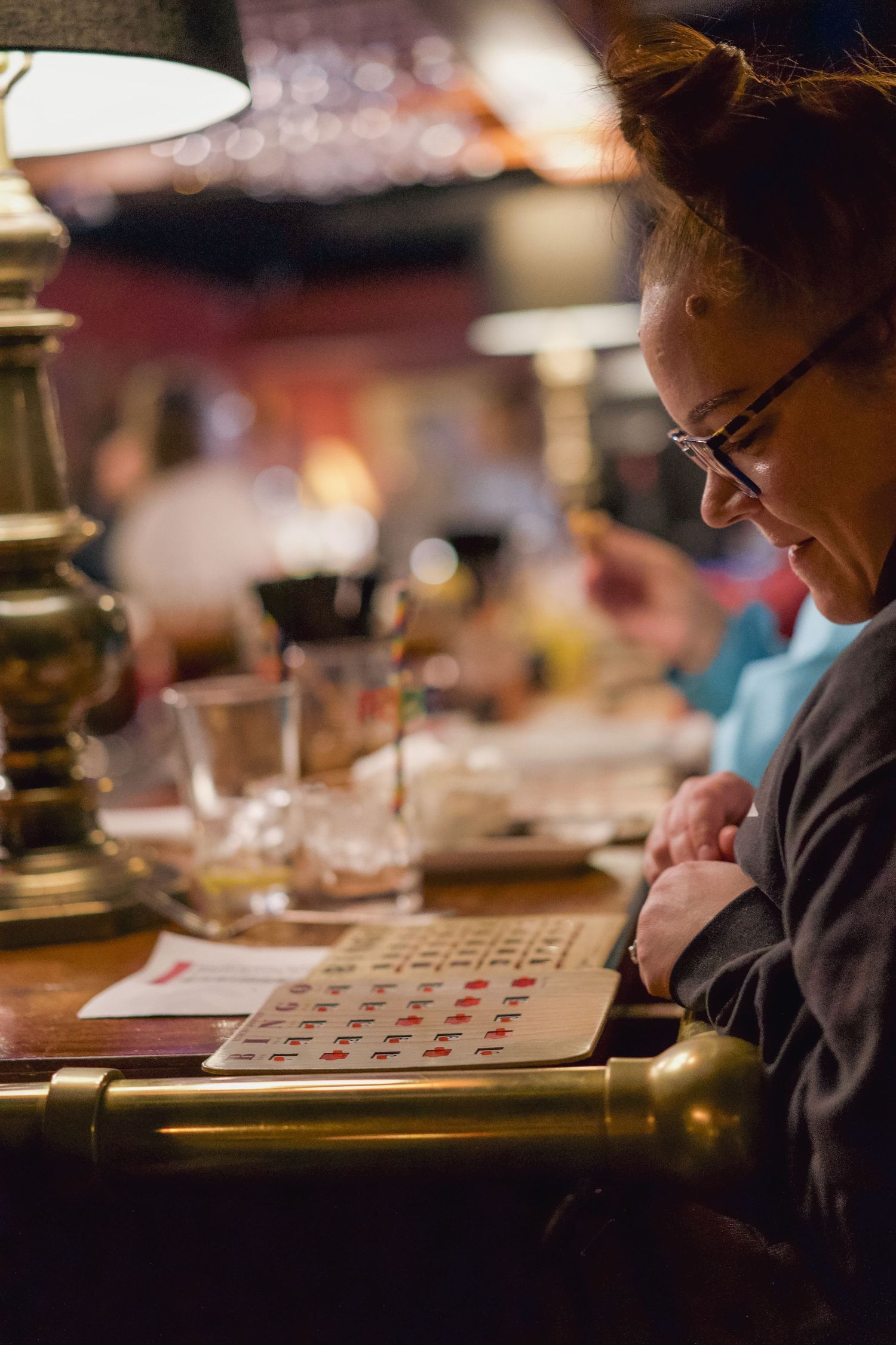 Woman with glasses concentrating on a bingo card at a dimly lit restaurant table.
