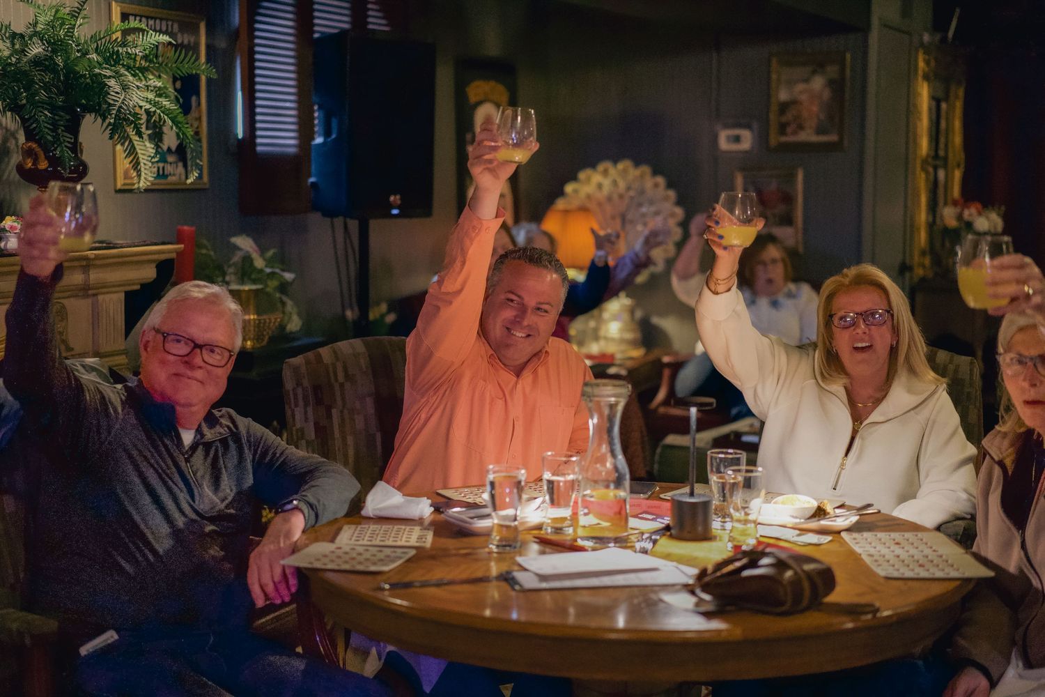 Group of happy adults raising glasses in a toast at a dimly lit restaurant bar celebration dinner.