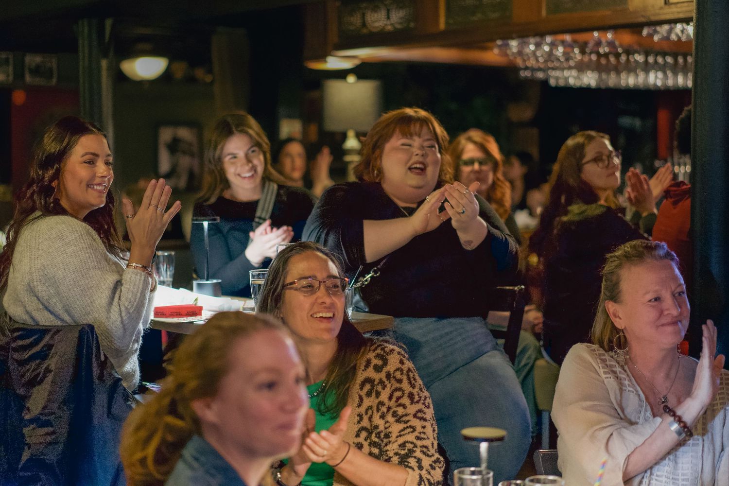 Excited women clapping and laughing together in a lively bar setting during a fun evening event.