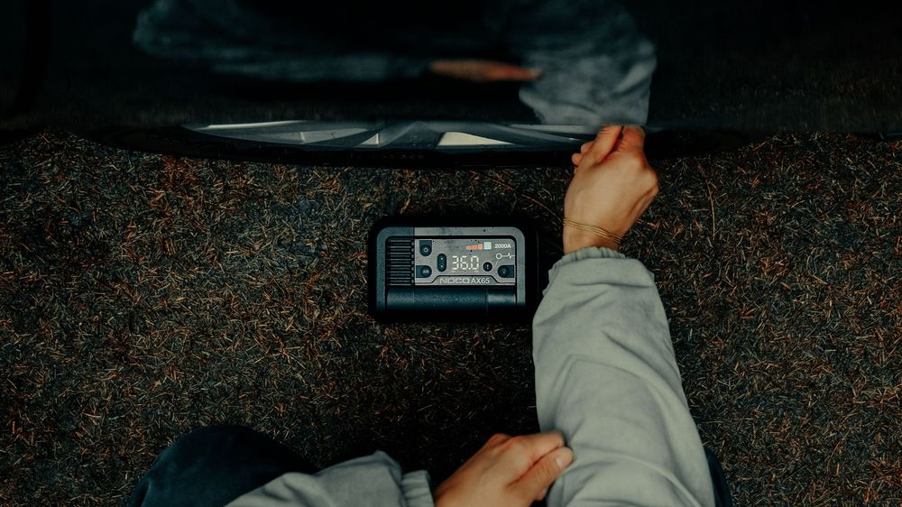 Overhead view of person holding a portable power station device while sitting on carpet floor.
