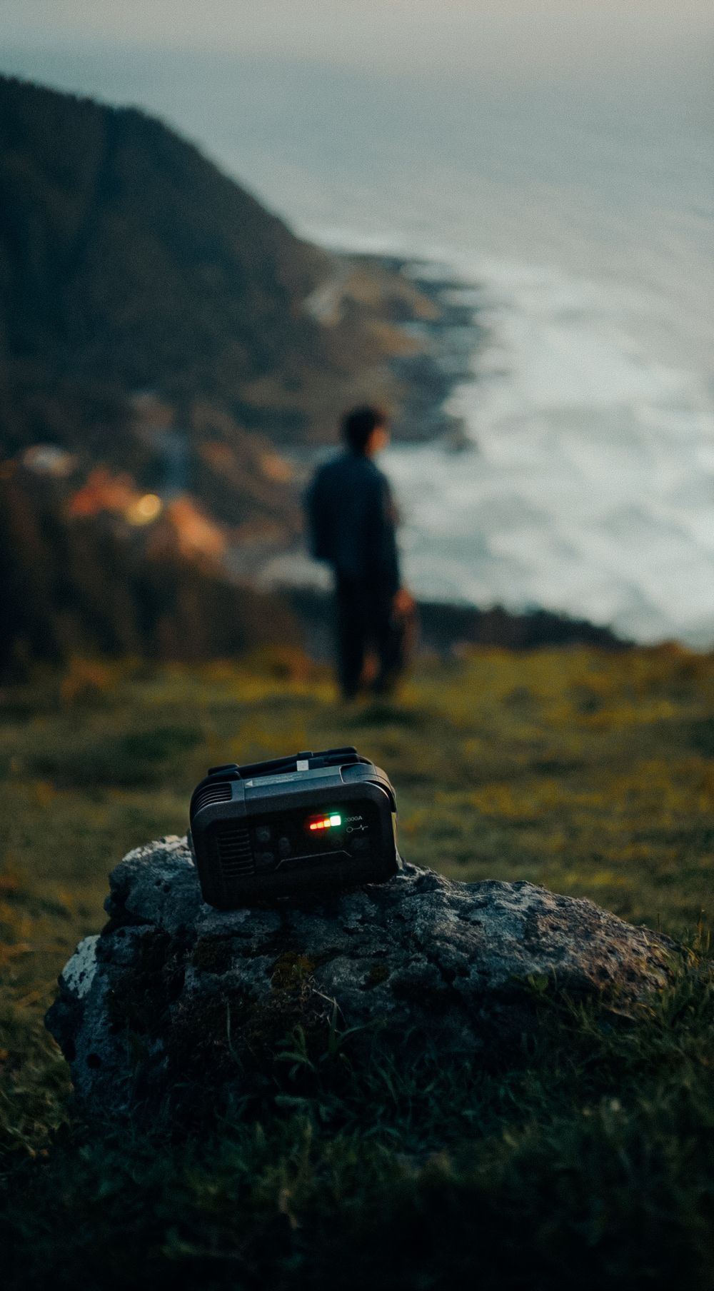 Portable power station on a rock with a person standing on a coastal cliff at dusk.