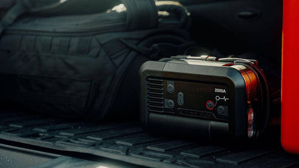 A portable power station sitting in the trunk of a vehicle next to a bag.
