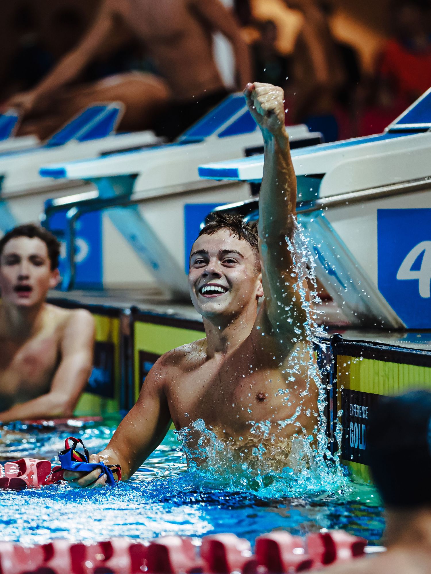 Young male swimmer celebrates victory in pool, raising fist triumphantly, smiling with joy at competitive swim meet.